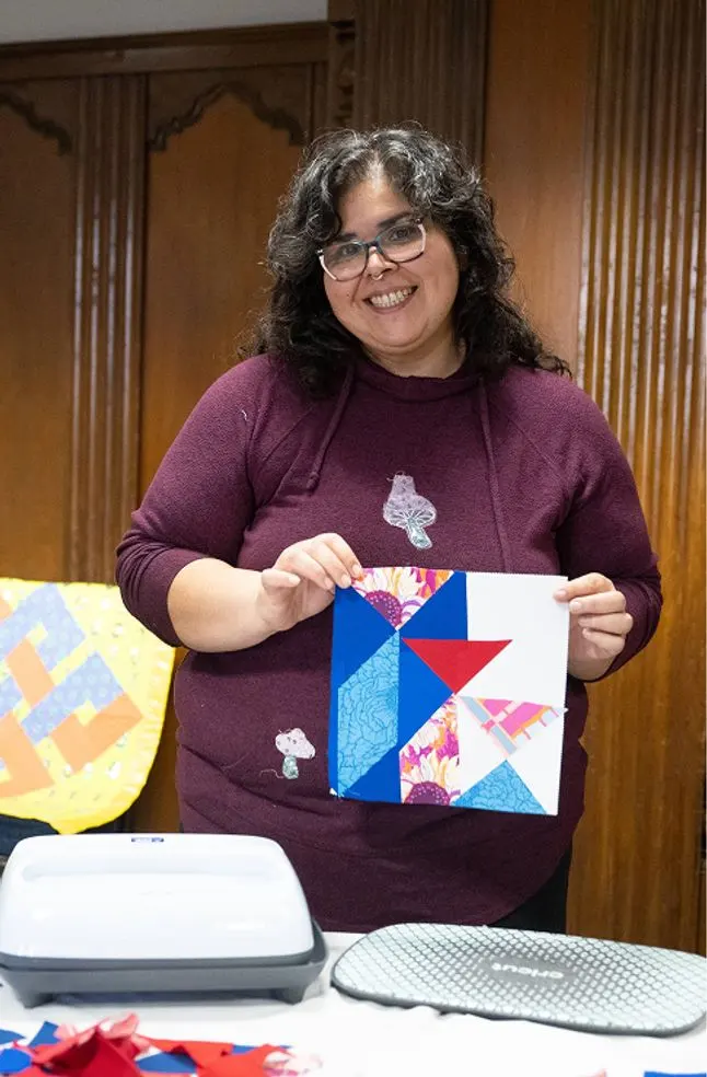 A student holds up their part of a quilt