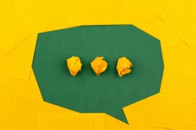 orange sheets of paper lie on a green school board and form a chat bubble with three crumpled papers.